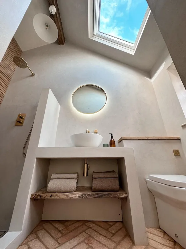 Çatı penceresi altındaki yuvarlak aynalı lavabo alanında microcement duvar