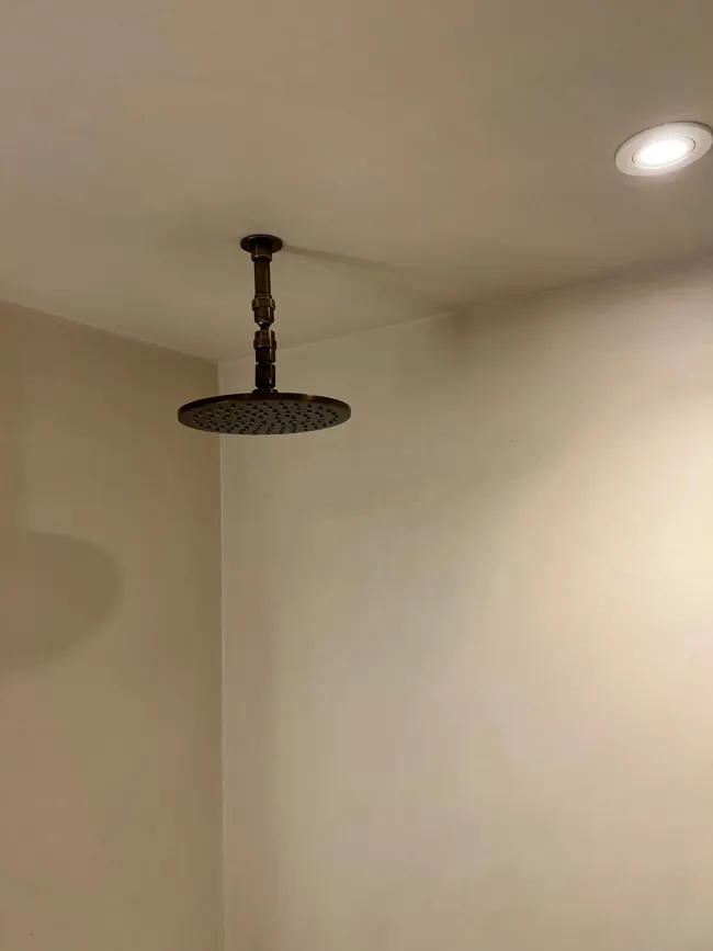 Siyah tepe duşu arkasında açık tonlu microcement duvar