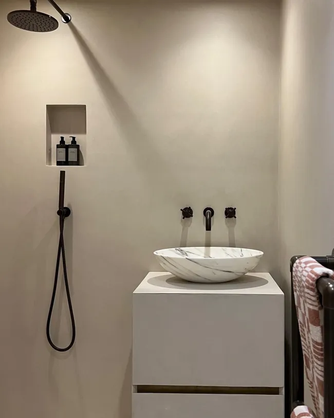 Siyah duş armatürü ve lavabo arkasında açık tonlu microcement duvar