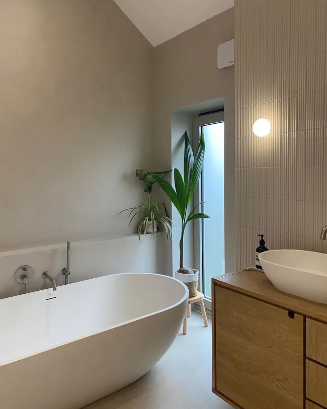 Küvet ve ahşap lavabo dolabı çevresinde açık tonlu microcement yüzeyler
