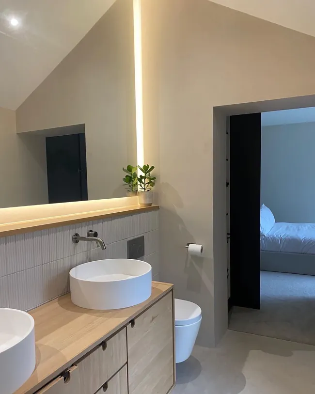 Yuvarlak lavabolu tezgâh arkasında açık tonlu microcement duvar