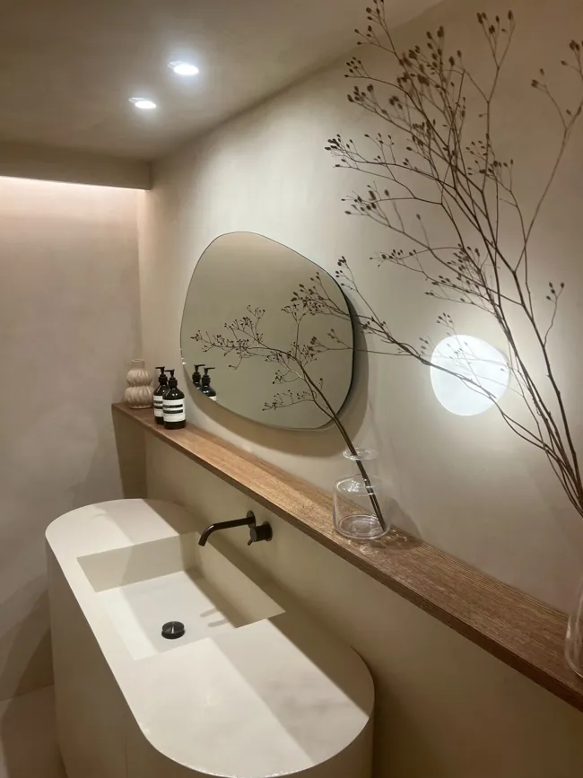 Yuvarlak ayna ve lavabo çevresinde açık tonlu microcement duvar