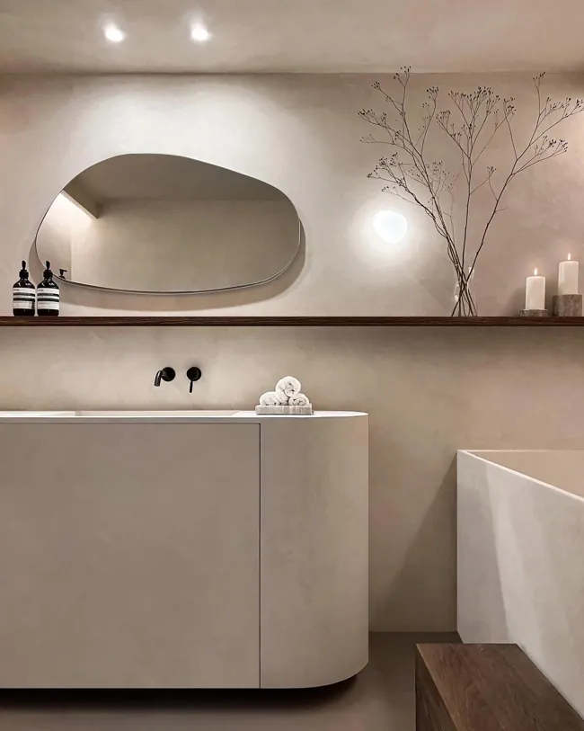 Oval aynalı lavabo alanında açık tonlu microcement duvar yüzeyi
