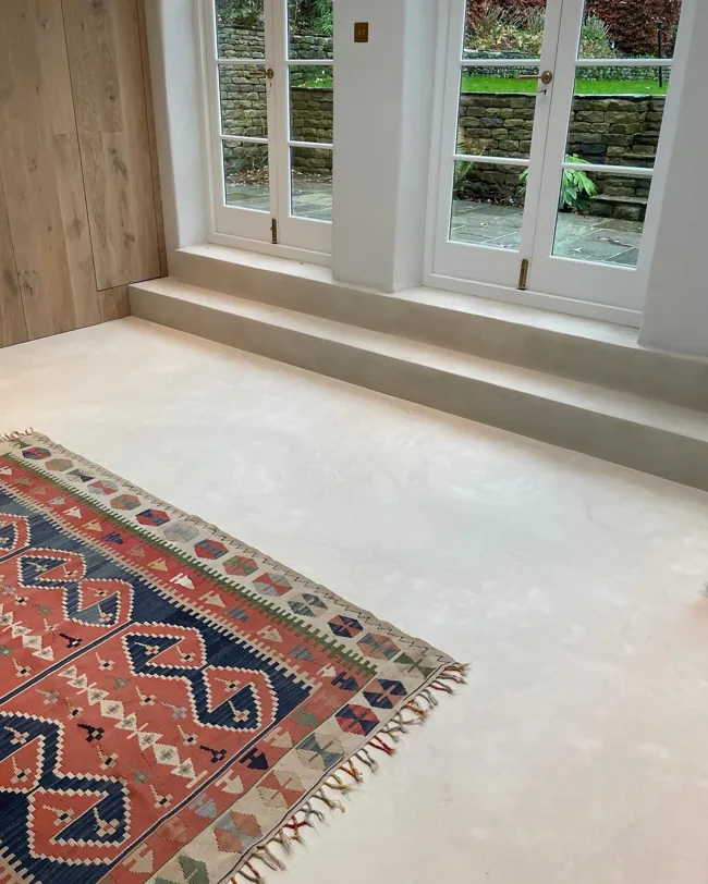 Büyük pencereler ve halı çevresinde açık tonlu microcement zemin