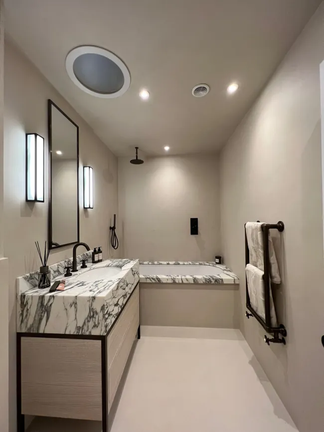 Uzun lavabo tezgâhı ve yuvarlak aynanın bulunduğu banyoda microcement yüzeyler
