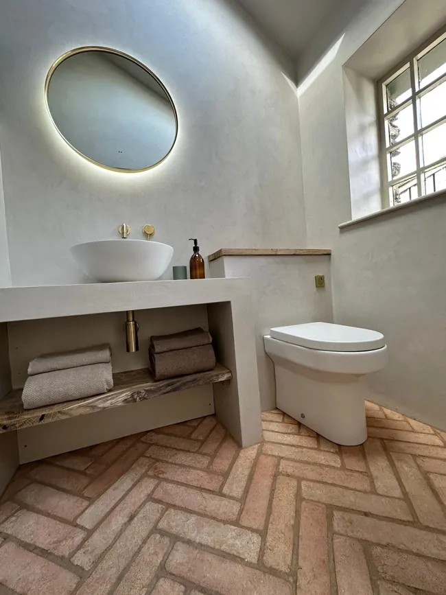 Yuvarlak ayna ve ahşap lavabo tezgâhı arkasında açık tonlu microcement duvar